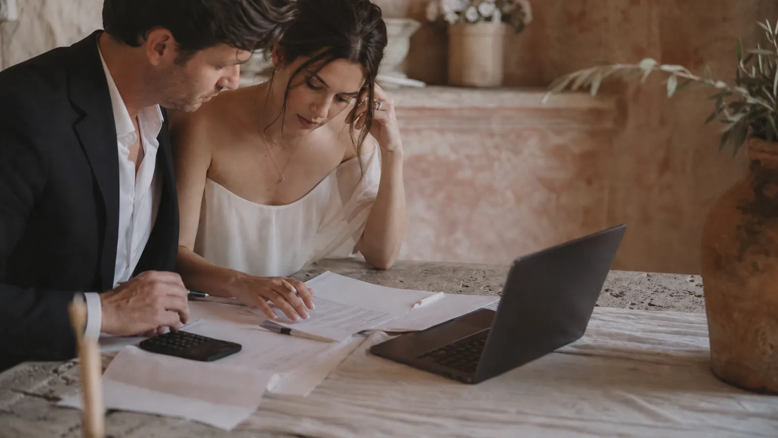 A couple's hands working through a wedding budget on paper and a laptop