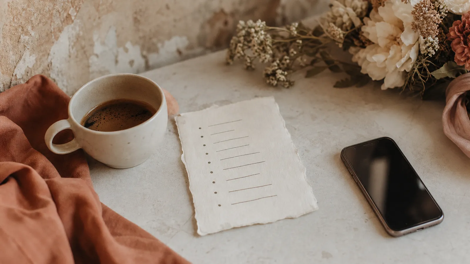 A short handwritten week-of wedding checklist beside a coffee and a phone