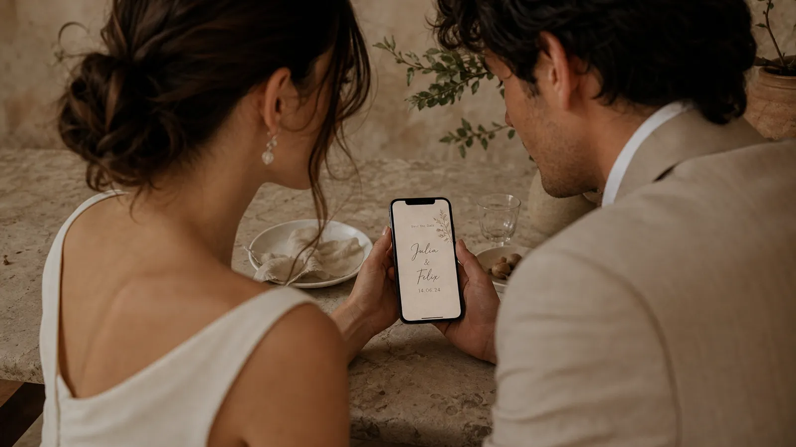 A save-the-date on a phone with handwritten-style text reading the couple's names and date